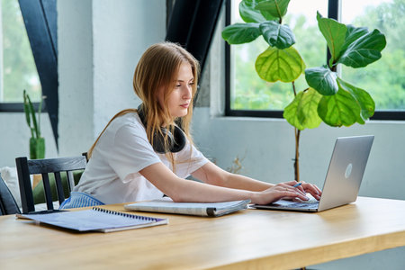 Young teenager girl college student sitting at desk with laptop, typing writing studying