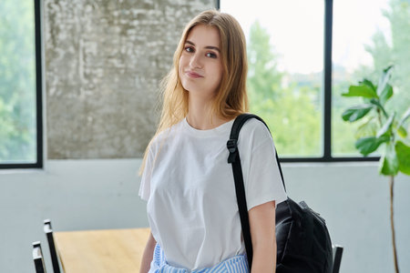 Portrait of student girl, positive smiling beautiful blonde with backpack looking at camera