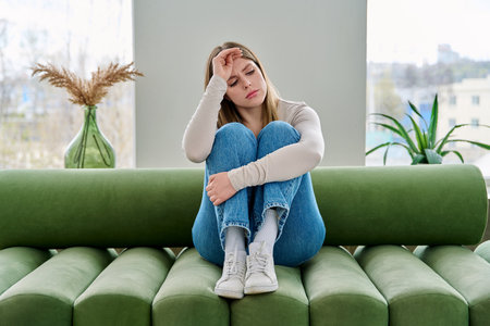 Unhappy upset young woman sitting on sofa at home, face close-upの写真素材