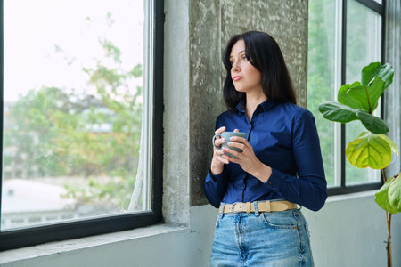 Serious tired, stressed woman standing near window