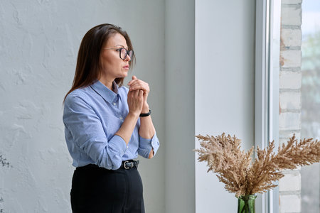 Mature tired, stressed woman standing near windowの写真素材