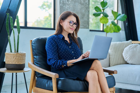 Portrait of middle aged woman typing on laptop sitting in chairの写真素材