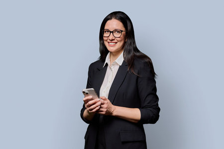 Portrait of successful middle-aged businesswoman with smartphone on light backgroundの写真素材