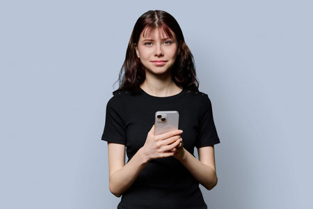 Portrait of female high school student with smartphone on gray background