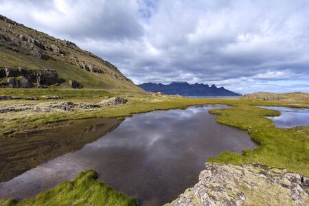 A small lake in which the mountains are reflected in the wild nature in the south of Iceland nearby Streitisviti Lighthouse, Icelandの写真素材