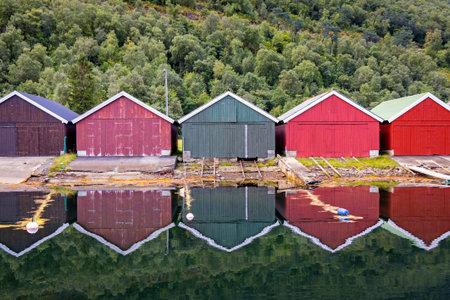 Colorful boathouses in the haven of Stordal with beautiful reflections and the mountains in...