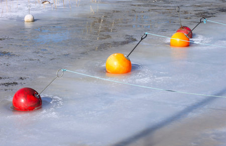 View in a small harbor in winter. The water is frozen. You can see some plastic buoys. Seen in...
