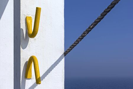 Two metal hooks on a wall on a ship. A rope casts a shadow. In the background you can see the ocean and the sky, all in blue.の写真素材