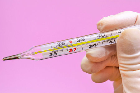 close up hand in a white latex glove with a mercury thermometer on a pink background. temperature...