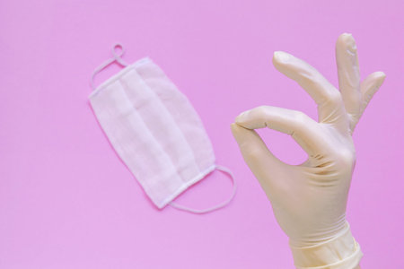 Protective face mask or medical mask in hand protected by white gloves on pink background....