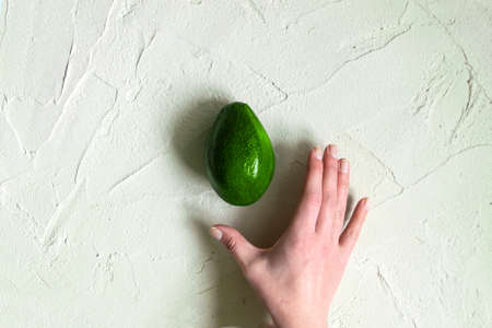 Fresh ripe avocado female hand on concrete background. Minimalism and objects top view. Organic healthy food, summer food concept. Useful product for female body and skin, used in beauty industryの写真素材