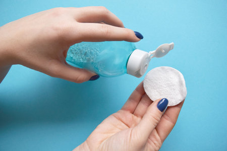 Woman's hand hold cotton pad and tonic on a blue background. Beauty concept, clean cosmetics. Copy...