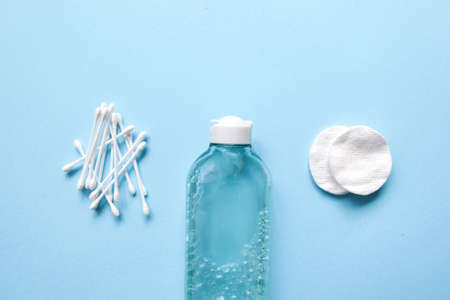 Set of cosmetic products on blue color background. Cotton pads, cotton sticks, bottle, makeup remover, micellar water, wash gel. Skin care for the face make-up remover. Minimalism flat lay with space for text.の写真素材