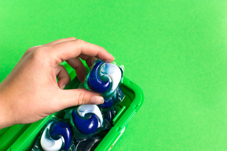 Capsules in hand for washing clothes isolated on green background. Housework concept. Washing and...