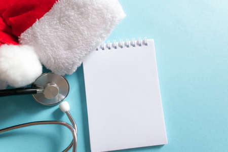 Medical Christmas and New year composition with stethoscope, notepad and Santa hat on blue background. Health care and medicine concept for card, calendar, cover. Copy space for text, flat lay.の写真素材