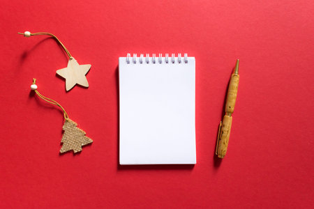 Notebook and pen on a red background, spiral notepad with christmas tree and star on a table. space...