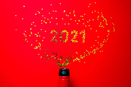 Small golden stars in the form of number 2021 a bottle of champagne on red background. Christmas,...