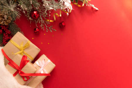 Beautiful Christmas composition with gift box tied with a ribbon, presents, Santa hat and fir branches on red background. Flat lay with copy space.の写真素材