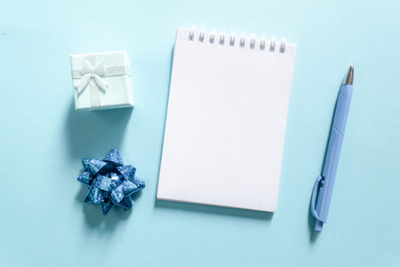 Notebook and pen on a blue background, spiral notepad with gift on a table. space for your text,...