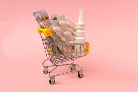 Shopping grocery cart with medicament, tablet, spray, thermometer on pink background. Concept of healthy care, business, shopping, sales. Space for textの写真素材