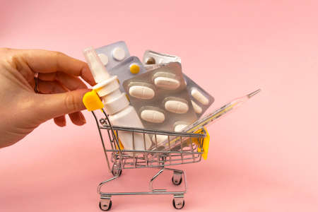 Shopping grocery cart with medicament, tablet, spray, thermometer and hand on pink background. Concept of healthy care, business, shopping, sales. Space for textの写真素材