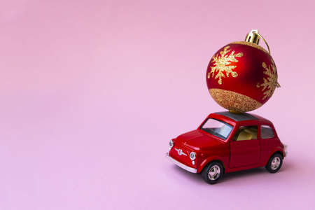 Minsk, Belarus, 23 november 2020. Concept christmas background. Red retro toy car delivering Christmas or New Year gifts, ball, on pink background. Merry Chrisymas and Happy New Year.の写真素材