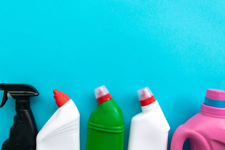 House cleaning supplies on blue background. Row of plastic bottles with cleaning liquid and sponges....