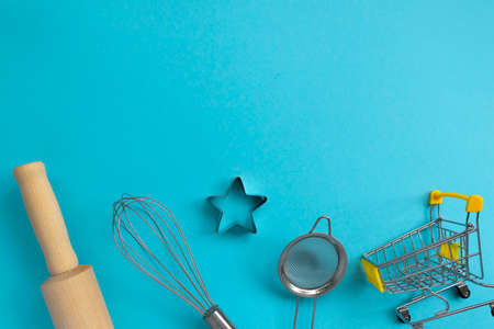Different baking tools with shopping grocery cart on blue background, top view. Baking and cooking ingredients shopping conceptの写真素材
