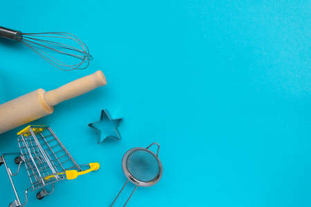 Different baking tools with shopping grocery cart on blue background, top view. Baking and cooking ingredients shopping conceptの写真素材