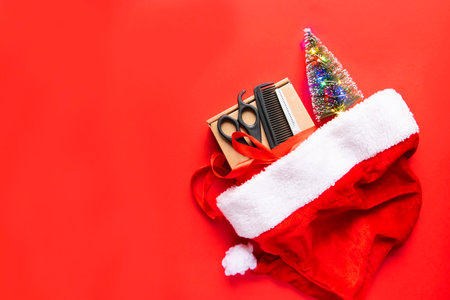 Flat lay Christmas composition. Hairdressing tools, gift and Christmas decor in a Santa Claus hat on a red background. Xmas, happy new year. copy space.の写真素材