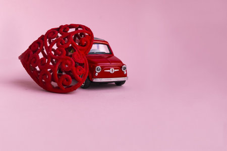 Pink retro toy car delivering bouquet red heart gift on pink background. February 14 card, Valentines day. 8 March, International Happy Womens Day.の写真素材