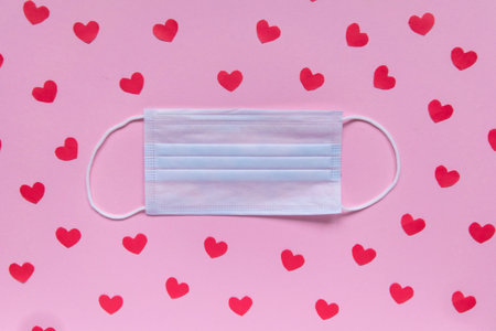 Creative flat lay Valentines Day composition. Medical face mask decorated with red hearts on pink...