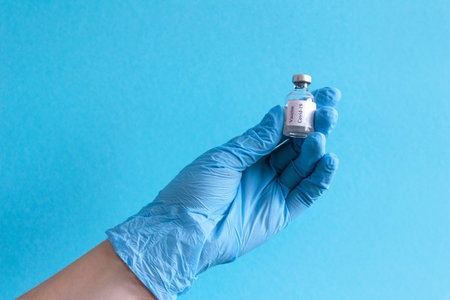 Hand in protective blue gloves hold medicine bottle of vaccine on blue background. Concept of vaccination and healthcare. Space for textの写真素材
