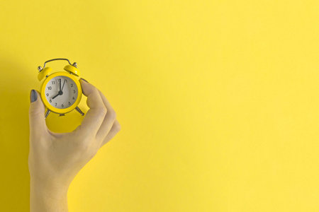 Ringing twin bell vintage classic alarm clock in female hand isolated on yellow background. Rest...