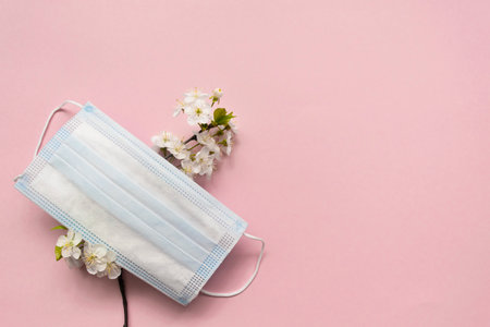 Seasonal spring summer allergy flowers concept. White cherry flowers with medical protective mask on pink background. Creative flat lay composition, copy spaceの写真素材
