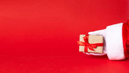 white gift box with red ribbon bow in santa hand on red background.の写真素材