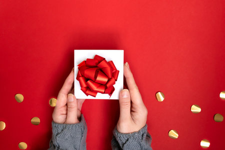 hands holding white gift box with red ribbon bow on red background. present for Christmas, new year, valentine day, copy spaceの写真素材