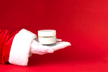 white cream bottle in santa hand on red background. present for Christmas, new year, copy spaceの写真素材
