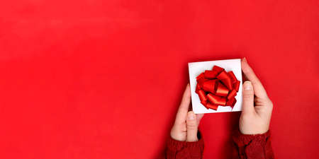 hands holding white gift box with red ribbon bow on red background. present for Christmas, new year, valentine dayの写真素材