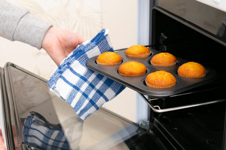 Caucasain woman holding tray with freshly made cupcakes or maffins at the kitchenの写真素材