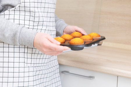 Caucasain woman holding tray with freshly made tasty cupcakes or muffins at the kitchen