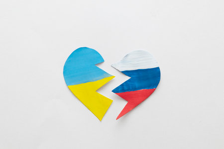 The concept of ending the war in Ukraine. Broken heart in the colors of the flag of Ukraine and Russia in female handsの写真素材