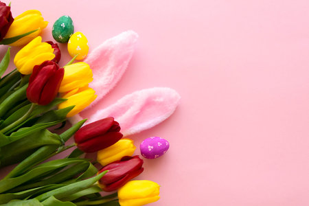 beautiful tulips, decorated Easter eggs and bunny ears on color pink background, top view