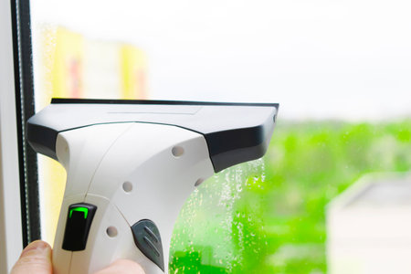 Window cleaning with glass cleaner. Mans hand holding a windshield wiper.Hand washes the window with...