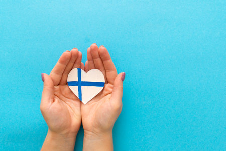 Paper heart in the colors of the flag of Finland in female hands on color blue backgroundの写真素材