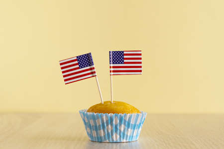 Homemade cupcake with USA flag on beige wood background. Holiday Independence Day. American flag decorates cakes. 4th of July party dessert.の写真素材