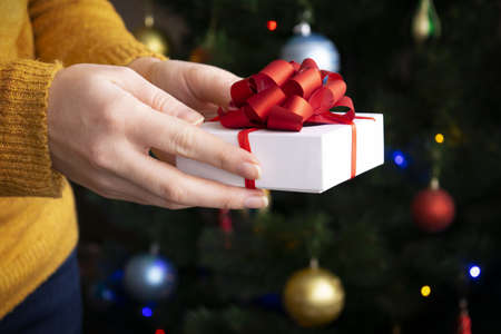 Hands holding little christmas gift with red bow on background with blurred light. Close up. Christmas compositionの写真素材