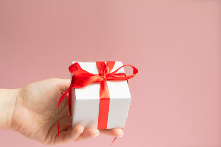 white gift box with red ribbon bow in woman hand with white sweater with copy space.の写真素材