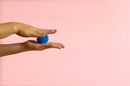 Womans hand with Spiny plastic blue massage ball on pink backgroundの写真素材