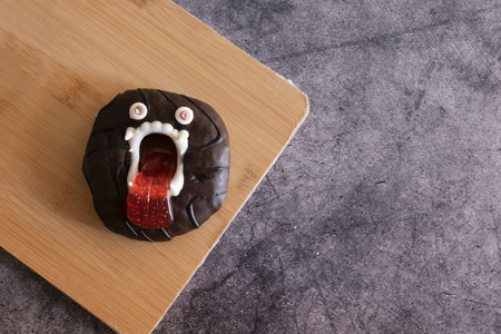 Scary halloween donut cake in chocolate glaze with teeth and eyes on concrete background for kids.Flat lay with copy spaceの写真素材